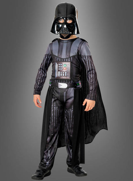 Ein Kind im „Darth Vader Kostüm Deluxe für Jungs“ – bestehend aus einem schwarzen Helm, einer Brustplatte, einem Umhang und Handschuhen –, das vor einem schlichten grauen Hintergrund steht.