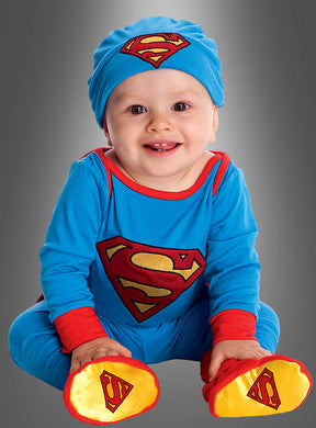 Das Baby sitzt fröhlich da und trägt das offiziell lizenzierte Superman-Babykostüm – bestehend aus einem blauen Anzug mit roten und gelben Superman-Logo-Details auf der Brust, der Mütze und den Füßen – vor einem grauen Hintergrund. Dieses offiziell lizenzierte DC-Kostüm ist das ideale Superhelden-Outfit für Ihren kleinen Helden.
