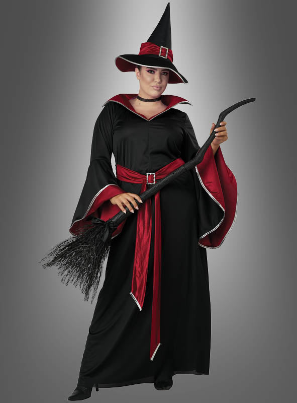 Eine Person, die das „Glamour Hexe Ruby Übergröße“-Kostüm mit spitzem Hut trägt und einen Besen in der Hand hält, steht vor einem schlichten grauen Hintergrund.