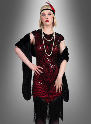 Eine Frau, die das „Hochwertiges Gatsby Kleid Daisy“ trägt – ein rot-schwarzes Kleid im Stil der 1920er Jahre mit Fransen –, ergänzt durch eine lange Perlenkette, ein Haarreif mit Federn und einen schwarzen Schal, steht vor einem grauen Hintergrund mit Farbverlauf.