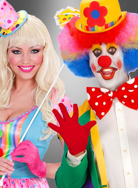 Eine Frau in einem pastellfarbenen Clownskostüm mit kurzen Handschuhen in verschiedenen Farben steht neben einem Mann in einem bunten Karnevalskostüm, komplett mit roter Nase, roter Perücke und gelbem Hut; beide lächeln in die Kamera.