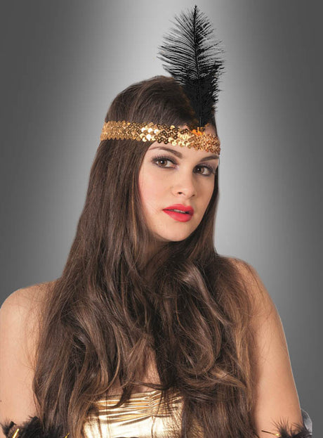 Eine Frau mit langen braunen Haaren trägt den „20er-Jahre-Haarschmuck mit schwarzer Feder“ – ein goldenes Haarband im Charleston-Stil mit Pailletten und einer schwarzen Feder –, dazu ein goldenes Oberteil, und posiert vor einem grauen Hintergrund mit Farbverlauf.