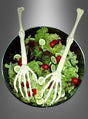 Eine Glasschüssel mit Salat aus Blattsalat, Kirschtomaten und Gurkenscheiben wird mit zwei „Salatbesteck Skeletthände“-Skeletthänden und -armen garniert.