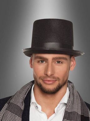 Ein Mann mit kurzem Bart trägt einen klassischen schwarzen Zylinder und einen karierten Frack über einem weißen Hemd und steht vor einem grau verlaufenden Hintergrund – ein Outfit, das perfekt für alle ist, die auf der Suche nach eleganten Karnevalskostümen sind.