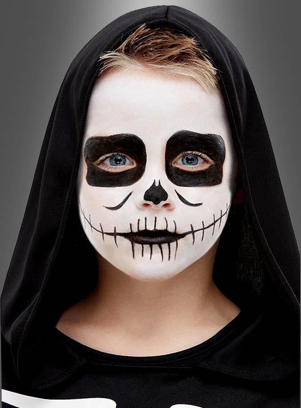 Ein Kind mit schwarzer Kapuze und Skelettkostüm, dessen Gesicht mit auffälliger weiß-schwarzer Totenkopf-Gesichtsbemalung geschminkt ist – die mit „Skelett Aqua Make-Up für Kinder“ für einen auffälligen Halloween-Look aufgetragen wurde –, blickt direkt in die Kamera.