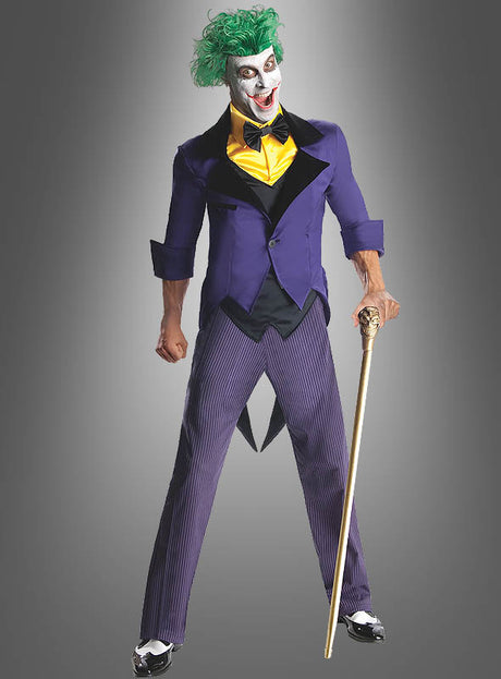 Eine Person trägt den Joker-Anzug für Herren, bestehend aus grünen Haaren, weißer Gesichtsbemalung, einem lila Sakko, einer gelben Weste und einer gestreiften Hose, hält einen goldenen Stock in der Hand und steht vor einem grauen Hintergrund.