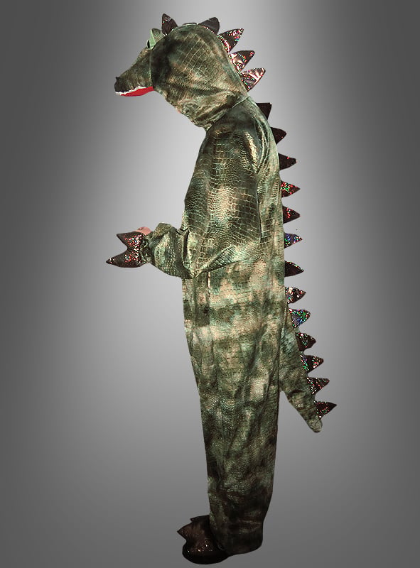 Eine Person, die ein grünes Dinosaurier-Kostüm für Erwachsene trägt, das mit einem Schwanz und Stacheln am Rücken versehen ist, steht seitlich vor einem grauen Hintergrund mit Farbverlauf.