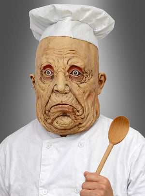 Eine Person in Kochuniform trägt die „Böse Zombie-Koch-Vollmaske“ – eine zerknitterte, übertrieben gestaltete Maske mit finsterem Blick – und hält einen Holzlöffel vor einem grauen Hintergrund in der Hand.