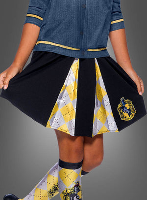 Ein Kind trägt ein blaues Hemd und den „Hufflepuff Rock für Kinder Harry Potter“, einen schwarz-gelben Faltenrock mit Argyle-Muster und offiziellem Wappen, dazu passende Socken – perfekt für alle Fans, die eine authentische Hufflepuff-Schuluniform suchen, die vom Harry-Potter-Kostümstil inspiriert ist.