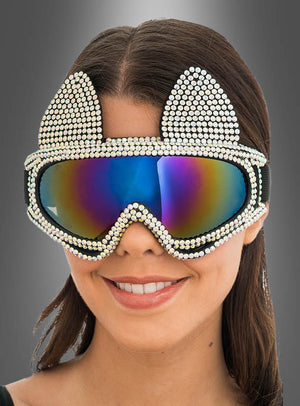 Vor einem grauen Hintergrund mit Farbverlauf lächelt eine Frau. Sie trägt die „2. Wahl – Ski Brille Katze Hüttenparty“, eine verspiegelte Skibrille mit Strassverzierungen und verspielten Katzenohren.