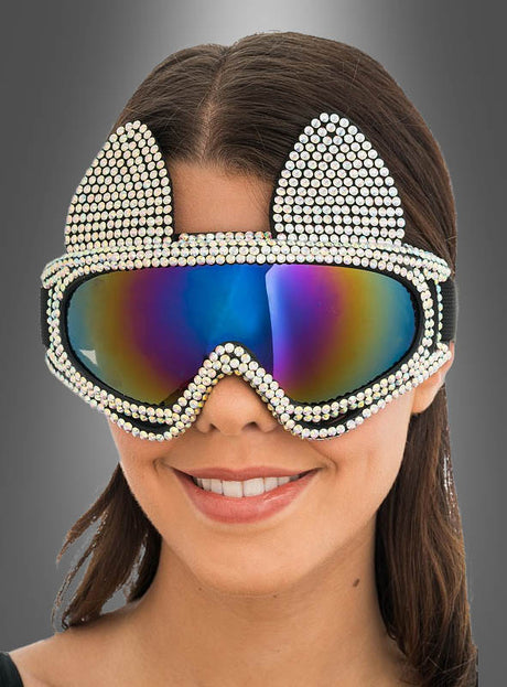 Vor einem grauen Hintergrund mit Farbverlauf lächelt eine Frau. Sie trägt die „2. Wahl – Ski Brille Katze Hüttenparty“, eine verspiegelte Skibrille mit Strassverzierungen und verspielten Katzenohren.