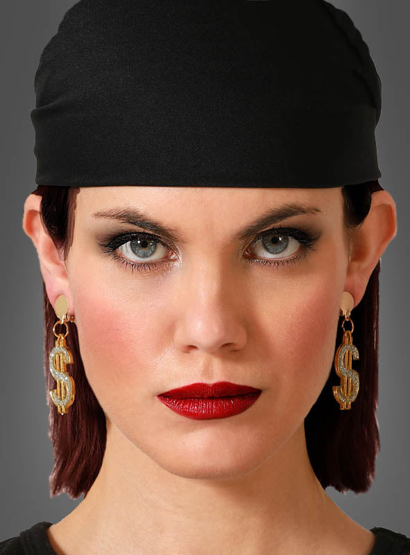 Eine Frau mit schwarzem Kopftuch, knallrotem Lippenstift und den „Dollar-Zeichen“-Ohrringen blickt mit ausdruckslosem Gesicht direkt in die Kamera.