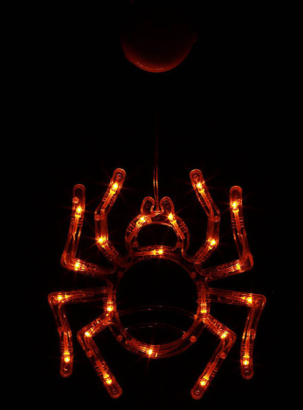 Eine leuchtende „Leuchtende Spinne“ (36 cm) mit LED hängt vor einem dunklen Hintergrund; ihr orangefarbener, spinnenförmiger Körper und ihre Beine werden von kleinen Glühbirnen beleuchtet.