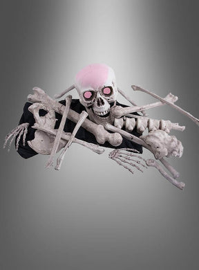 Ein menschliches Skelett-Knochenset mit LED-Schädel, dessen Augen rosa leuchten und das eine Schädelkappe trägt, liegt verstreut auf einem grauen Hintergrund mit Farbverlauf, wobei mehrere Kunststoffknochen über den Körper gekreuzt sind.