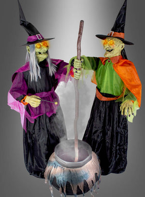 Zwei lebensgroße, animierte Hexen aus der Ausstellung „Zwei Hexen mit Kessel“, jeweils 180 cm groß und in bunte Roben und Hüte gekleidet, stehen um einen Kessel herum – eine von ihnen rührt mit einem langen Stab darin um.