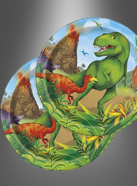 Zwei Pappteller „Pappteller Dino Party“ (17 cm) mit bunten Comic-Dinosauriern, Vulkanen und üppig grünen Pflanzen auf einem grauen Hintergrund mit Farbverlauf.