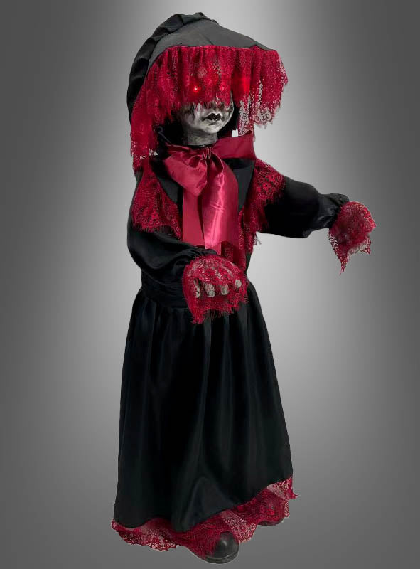 Die Halloween-Puppe „90 cm, gruselig animiert“ steht vor einem grauen Hintergrund mit Farbverlauf und trägt ein schwarzes Kleid mit roter Spitzenborte und einem Schleier. Sie hat leuchtende Augen, ein blasses Gesicht und ausgestreckte Hände.