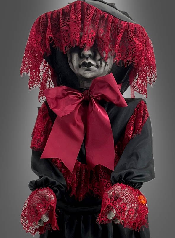 Eine 90 cm große, gruselig animierte Halloween-Puppe, die ein Kind darstellt, das schwarze Kleidung mit roten Spitzenakzenten, eine große rote Schleife und eine das Gesicht teilweise verdeckende Kapuze trägt und die Arme nach vorne ausgestreckt hat.