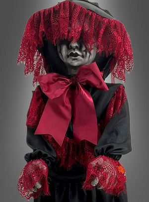 Eine 90 cm große, gruselig animierte Halloween-Puppe, die ein Kind darstellt, das schwarze Kleidung mit roten Spitzenakzenten, eine große rote Schleife und eine das Gesicht teilweise verdeckende Kapuze trägt und die Arme nach vorne ausgestreckt hat.