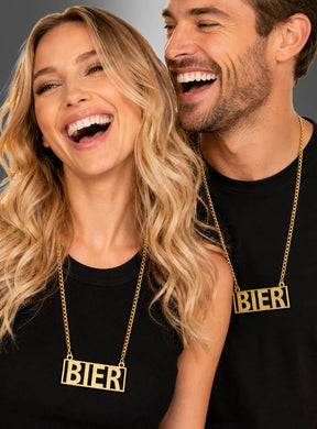 Zwei Menschen, die schwarze Oberteile und „Goldene Bierkette“-Partyschmuck-Halsketten mit dem Wort „BIER“ in großen Blockbuchstaben tragen, lächeln und lachen gemeinsam – ein perfektes Beispiel dafür, wie diese festliche Halskette jeder Feier eine fröhliche Note verleihen kann.