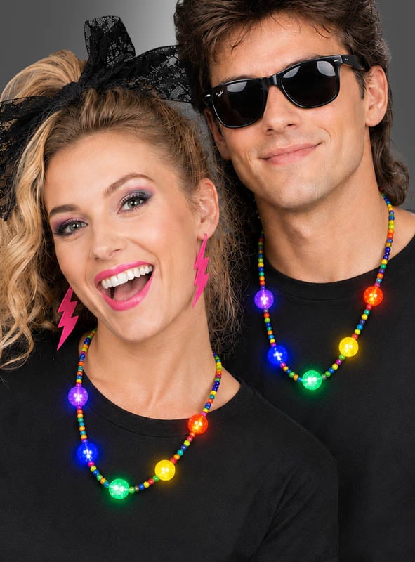 Zwei Personen in schwarzen T-Shirts, mit bunten Perlenketten wie der „Bunte LED-Partykette mit Licht“ und auffälligen Accessoires – darunter pinkfarbene Blitz-Ohrringe und dunkle Sonnenbrillen – lächeln und posieren vor einem schlichten Hintergrund.