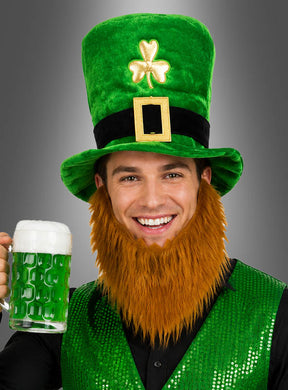 Eine Person, die den „St. Patrick’s Day Zylinder mit Bart“ trägt – einen großen grünen Koboldzylinder und einen orangefarbenen Bart – sowie eine grüne Paillettenweste, hält einen Krug mit grünem Bier in der Hand und lächelt in die Kamera.