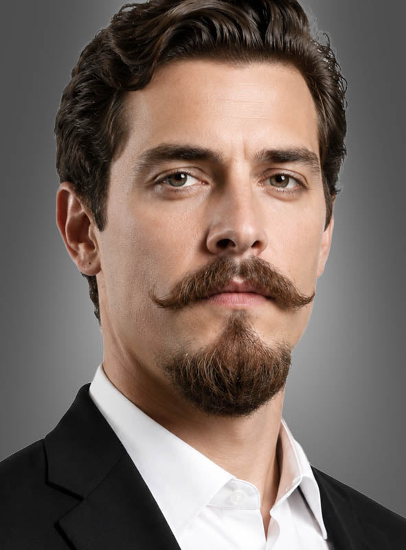 Ein Mann mit kurzen dunklen Haaren, einem gestylten Schnurrbart und einem Ziegenbart trägt ein schwarzes Sakko und ein weißes Hemd, während er vor einem schlichten grauen Hintergrund nach vorne blickt. Sein Look erinnert an ein Gentleman-Kostüm, das durch den Realistischen Bart für Herren unterstrichen wird und ihm ein elegantes und vornehmes Aussehen verleiht.