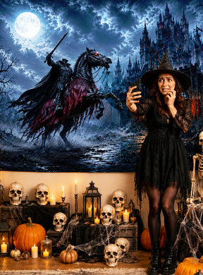 Eine Frau in einem Hexenkostüm macht ein Selfie, umgeben von Halloween-Dekorationen und auffälligen Wandbildern, vor dem dramatischen Fotohintergrund „Kopfloser Reiter“ (170 x 200 cm) aus Stoff, auf dem im Hintergrund ein kopfloser Reiter und eine Burg zu sehen sind.