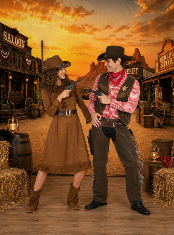 Zwei Personen in Cowboy-Kostümen richten Spielzeugpistolen aufeinander, während sie auf einem Holzboden stehen, auf dem die Wanddekoration „Große Westernstadt XXXL“ (300 x 500 cm) vor dem Hintergrund eines leuchtenden Sonnenuntergangs eine dramatische Westernstadt-Szene schafft.