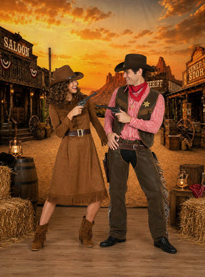 Zwei Personen in Cowboy-Kostümen richten Spielzeugpistolen aufeinander, während sie auf einem Holzboden stehen, auf dem die Wanddekoration „Große Westernstadt XXXL“ (300 x 500 cm) vor dem Hintergrund eines leuchtenden Sonnenuntergangs eine dramatische Westernstadt-Szene schafft.