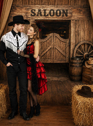 Ein Mann in Cowboy-Kleidung und eine Frau in einem roten Saloon-Kleid stehen gemeinsam vor dem „Western Saloon Fotohintergrund XXL 170 x 220 cm“, der einen mit Heuballen, Fässern und klassischen Western-Requisiten geschmückten Saloon-Eingang aus Holz zeigt – die perfekte Kulisse für jede Themenveranstaltung.