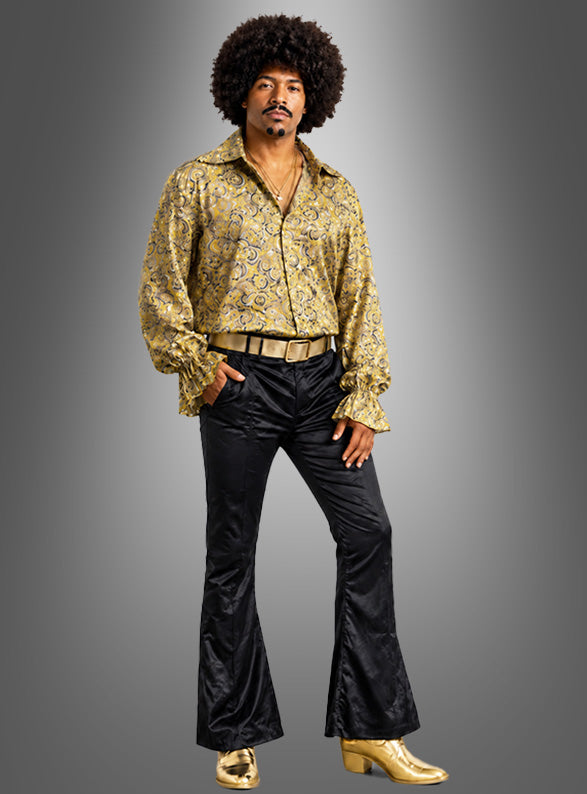 Ein Mann in einem von den 1970er Jahren inspirierten Outfit, bestehend aus einem gelb gemusterten „Flower Power“-Hemd für Herren, einer schwarzen Schlaghose, einem goldenen Gürtel, goldenen Schuhen und einer Afro-Frisur, der vor einem einfarbigen Hintergrund mit Farbverlauf steht.