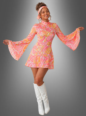Eine Frau in einem leuchtenden Neon-Hippie-Kleid für Damen mit Stirnband und weißen kniehohen Stiefeln steht vor einem grauen Hintergrund und präsentiert den perfekten Retro-Look der 1960er Jahre mit ausgestelltem Ärmel – eine Anspielung auf den klassischen Kostümstil der 70er Jahre.