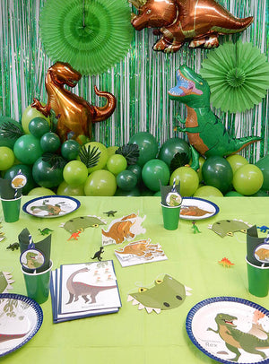 Das 81-teilige „Dino Party Deko“-Set für Kindergeburtstage umfasst einen mit grünen und goldenen Luftballons geschmückten Party-Tisch im Dinosaurier-Stil, Luftballons in Dinosaurierform, Partyhüte, Teller, Becher und lustige Dinosaurier-Dekorationen, die auf einer grünen Tischdecke arrangiert sind.