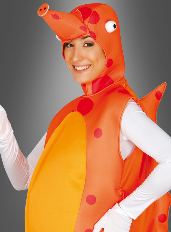 Eine Person lächelt, während sie das Seepferdchenkostüm für Erwachsene trägt – ein leuchtend orange-rotes Kostüm mit Punkten, das eine lange Schnauze und Flossen aufweist – und posiert vor einem grauen Hintergrund mit Farbverlauf.