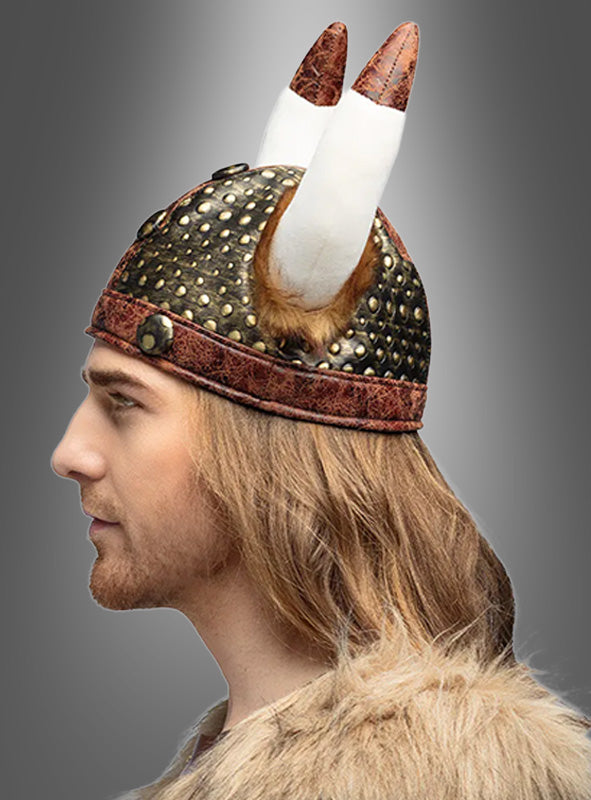 Eine Person im Profil, die einen Wikinger-Stoffhelm als Teil eines Nordmann-Kostüms trägt, ist in ein mit Pelz besetztes Outfit gekleidet und hat langes hellbraunes Haar; im Hintergrund ist ein grauer Farbverlauf zu sehen.