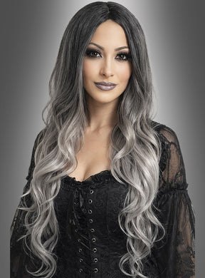 Eine Frau mit langen, welligen, schwarz-grauen Ombré-Haaren, gestylt mit der Perücke „Geisterdame graue Langhaarperücke“, die ein schwarzes Schnürkleid trägt und vor einem grauen Hintergrund mit Farbverlauf posiert.