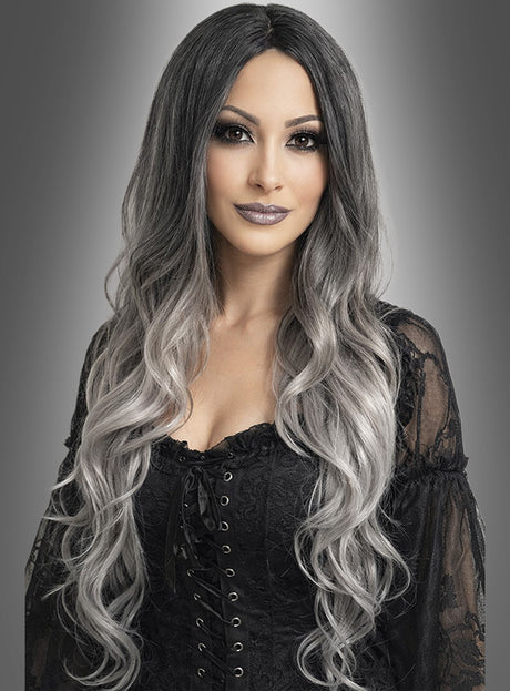 Eine Frau mit langen, welligen, schwarz-grauen Ombré-Haaren, gestylt mit der Perücke „Geisterdame graue Langhaarperücke“, die ein schwarzes Schnürkleid trägt und vor einem grauen Hintergrund mit Farbverlauf posiert.