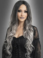 Eine Frau mit langen, welligen, schwarz-grauen Ombré-Haaren, gestylt mit der Perücke „Geisterdame graue Langhaarperücke“, die ein schwarzes Schnürkleid trägt und vor einem grauen Hintergrund mit Farbverlauf posiert.