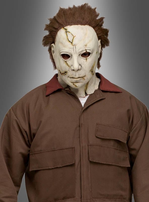 Eine Person im Michael-Myers-Kostüm aus „Halloween“ – weiße, gestrichelte Maske mit braunen Haaren und braunem Overall vor grauem Hintergrund – die perfekte gruselige Halloween-Kostümidee oder Verkleidung für einen Horrorfilm.