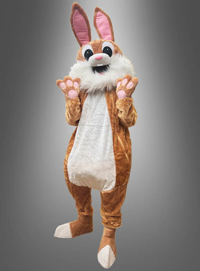 Eine Person trägt das waschbare Hasen-Maskottchen-Komplettkostüm in Größe L in den Farben Braun und Weiß mit großen Ohren, rosa Pfoten, einem flauschigen Schwanz und einer Vollmaske und steht dabei vor einem grauen Hintergrund mit Farbverlauf.