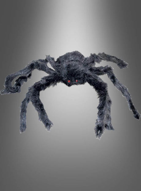 Eine schwarze, pelzige Kunstspinne mit roten Augen ist vor einem schlichten grauen Hintergrund mit Farbverlauf abgebildet – ideal als Ergänzung zu Ihrer „Spinne 30–90 cm“-Halloween-Dekokollektion oder als auffällige „Riesige Spinnen“-Halloween-Dekoration.