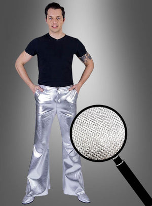 Ein Mann in einem schwarzen Hemd und einer glänzenden silbernen Disco-Schlaghose im Stil der 70er Jahre steht mit den Händen in den Taschen da. Ein vergrößerter Kreis hebt die metallische Struktur der Hose hervor und betont deren ikonisches Retro-Design vor einem grauen Hintergrund mit Farbverlauf.
