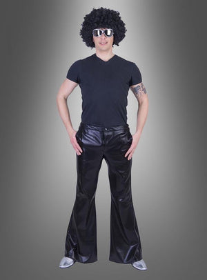 Eine Person mit schwarzer Perücke, Sonnenbrille, schwarzem T-Shirt, glänzender Disco-Schlaghose im Stil der 70er Jahre und silbernen Schuhen steht vor einem grauen Hintergrund mit Farbverlauf – perfekt für jede Karnevals- oder 70er-Jahre-Mottoparty.