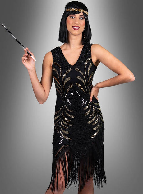 Eine Frau, gekleidet in das glamouröse Flapper-Kleid „Vivian“ in Schwarz und Gold, ergänzt durch ein passendes Stirnband und mit einer Zigarettenspitze in der Hand, steht vor einem grauen Hintergrund mit Farbverlauf – ein eindrucksvolles Beispiel für Damenkostüme im Stil der 20er Jahre.