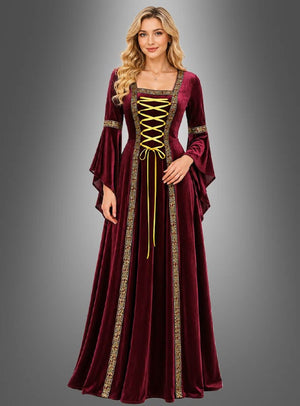 Eine Frau in einem burgunderroten Mittelalterkleid „Hildegard“ – rot oder grün – mit Goldstickerei und einer gelben Schnürung vorne (Kleid mit Schnürung), die vor einem grauen Hintergrund mit Farbverlauf steht.