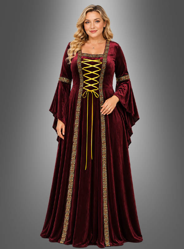 Eine Frau, die das Mittelalterkleid „Hildegard“ in Rot mit goldenen Verzierungen und einer Schnürung vorne trägt, steht vor einem schlichten grauen Hintergrund mit Farbverlauf.