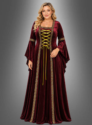 Eine Frau, die das Mittelalterkleid „Hildegard“ in Rot mit goldenen Verzierungen und einer Schnürung vorne trägt, steht vor einem schlichten grauen Hintergrund mit Farbverlauf.