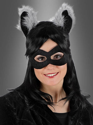 Eine Person in einem schwarzen Katzenkostüm – komplett mit Maske und pelzigen Ohren – lächelt vor einem grauen Hintergrund in die Kamera und liefert damit eine lustige Inspiration für alle, die auf der Suche nach einzigartigen Tierkostümen für Erwachsene oder Alternativen zum klassischen Waschbär-Set mit Ohren, Augenmaske und Schwanz sind.