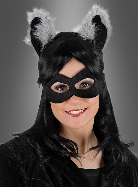 Eine Person in einem schwarzen Katzenkostüm – komplett mit Maske und pelzigen Ohren – lächelt vor einem grauen Hintergrund in die Kamera und liefert damit eine lustige Inspiration für alle, die auf der Suche nach einzigartigen Tierkostümen für Erwachsene oder Alternativen zum klassischen Waschbär-Set mit Ohren, Augenmaske und Schwanz sind.